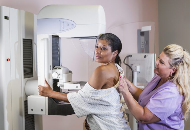 Woman receiving a mammogram with assistance from a technician.