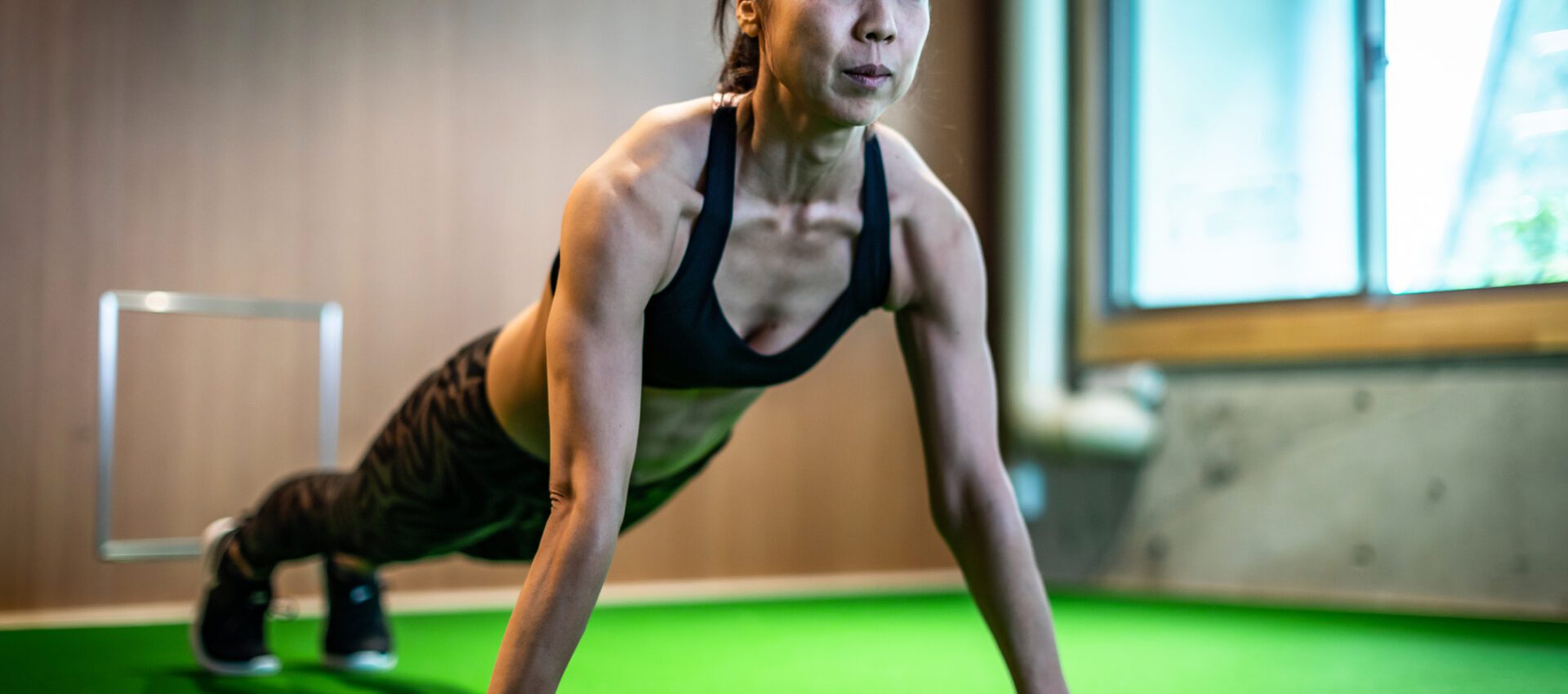 A woman performing push-ups on a green indoor surface, demonstrating strength and fitness.